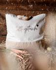 Helle Jutetasche mit schwarz-goldenem Motiv auf Stroh im Stall