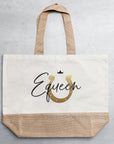 Helle Jutetasche mit schwarz-goldenem Motiv auf grauem Untergrund