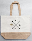 Helle Jutetasche mit schwarz-goldenem Motiv auf grauem Untergrund
