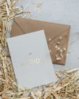 Postkarte neben Kraftpapier Umschlag auf Stroh und grauem Untergrund