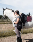 Junge Frau mit schwarzem Rucksack neben einem weißen Pferd