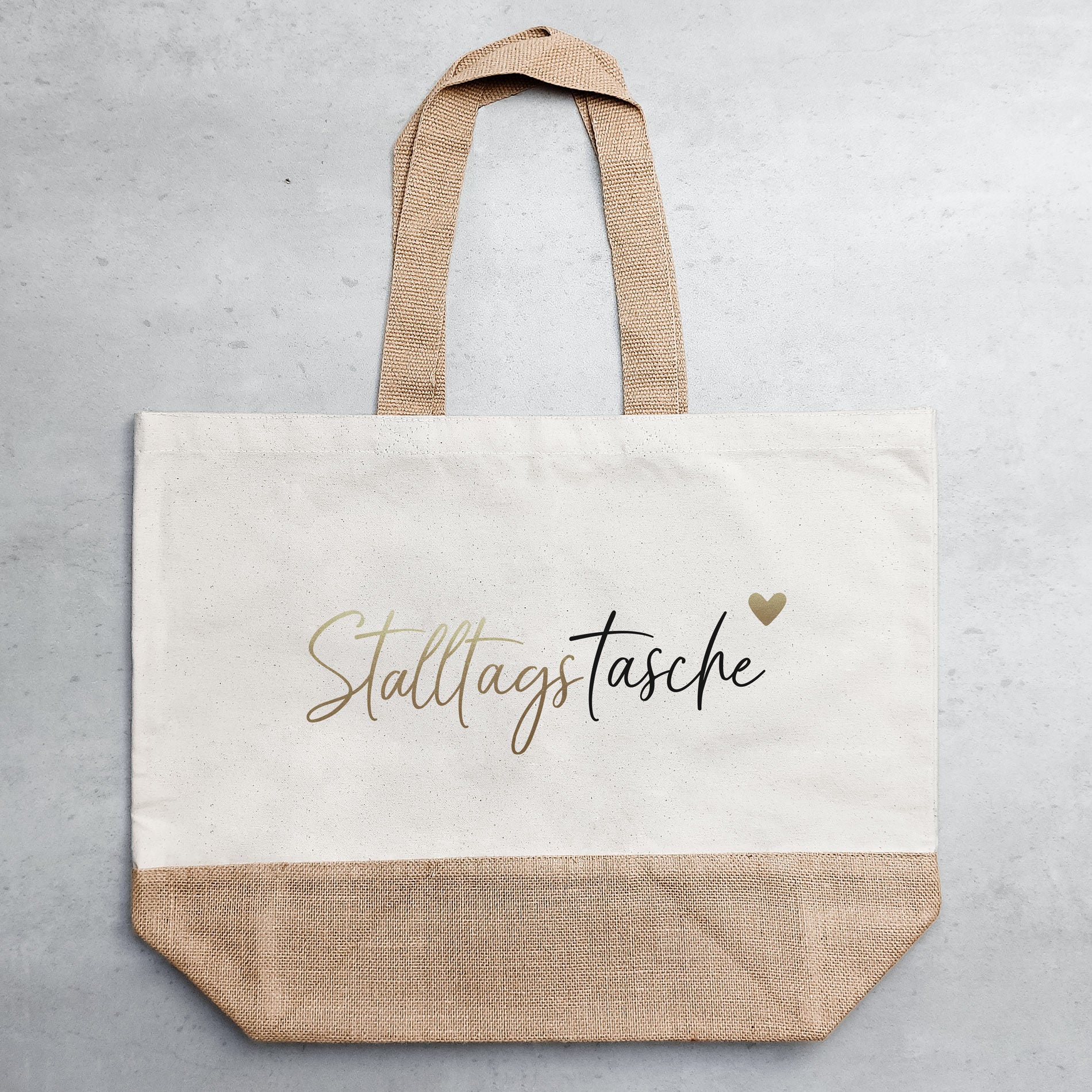 Helle Jutetasche mit schwarz-goldenem Motiv auf grauem Untergrund