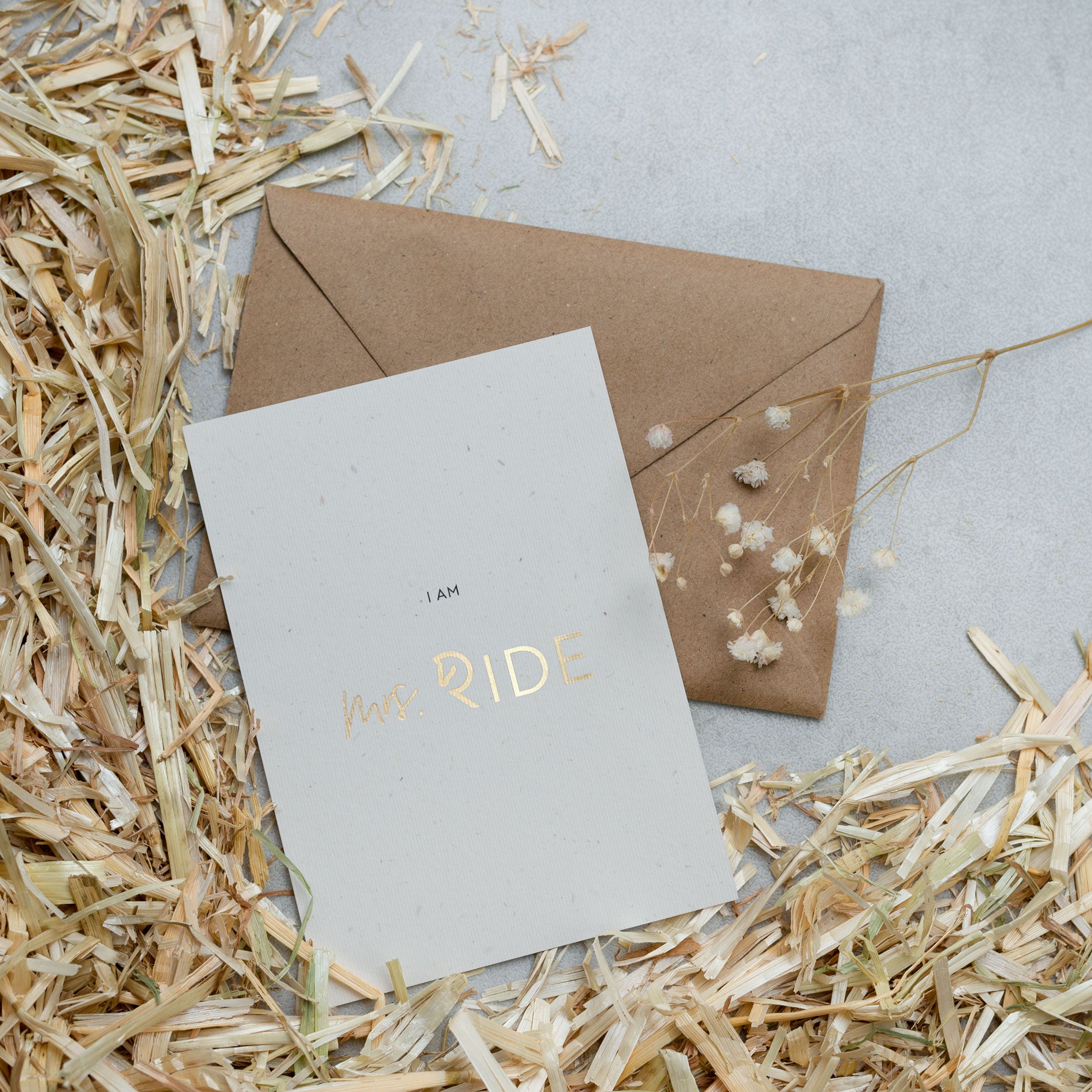 Postkarte neben Kraftpapier Umschlag auf Stroh und grauem Untergrund