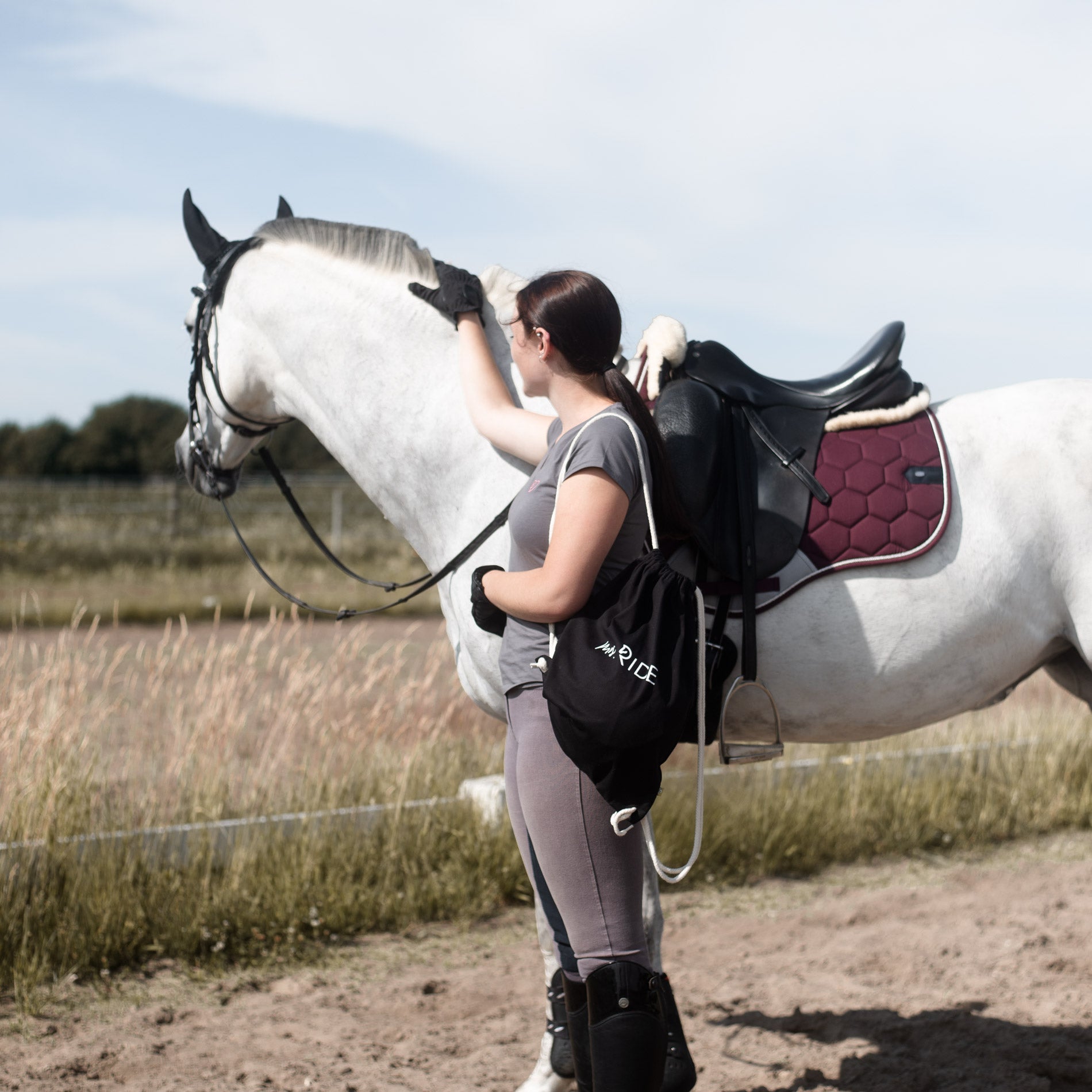 Junge Frau mit schwarzem Rucksack neben einem weißen Pferd 